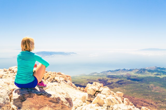 Young woman looking and meditation outside natural beautiful inspirational landscape environment, fitness and exercising motivation and inspiration in sunny mountains over blue sky and ocean sea.